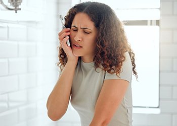 Woman experiencing discomfort while brushing her teeth