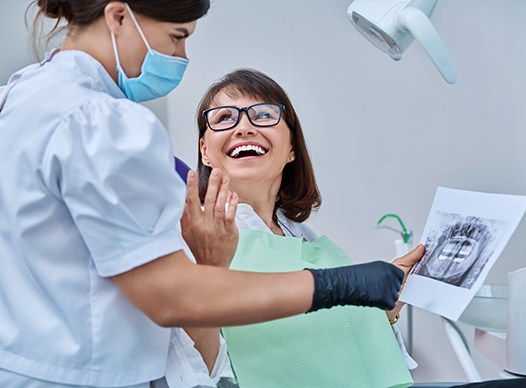 Woman smiling with dentist while reviewing X-ray