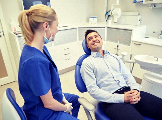 man sitting in dental chair and smiling at his dentist