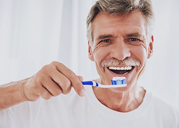 man in a white T-shirt brushing his teeth